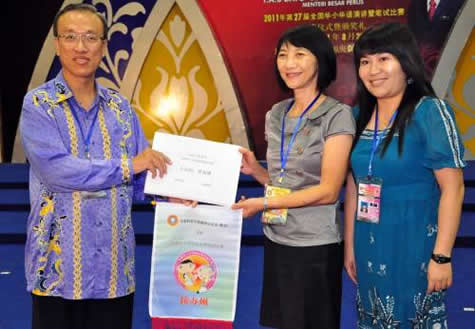 登嘉楼华校教师会主席邢孟兰（中）从玻璃市州华校教师会主席梁兆壮（左）手中接过2012年度全国华小华语演讲暨笔试比赛的主办权。右为登嘉楼州领队符芳玲。（照片来源：星洲日报）